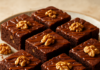 Καρύδινο brownie σοκολάτας σε κομμάτια με γυαλιστερή καραμέλα από πάνω, σε πιάτο σερβιρίσματος